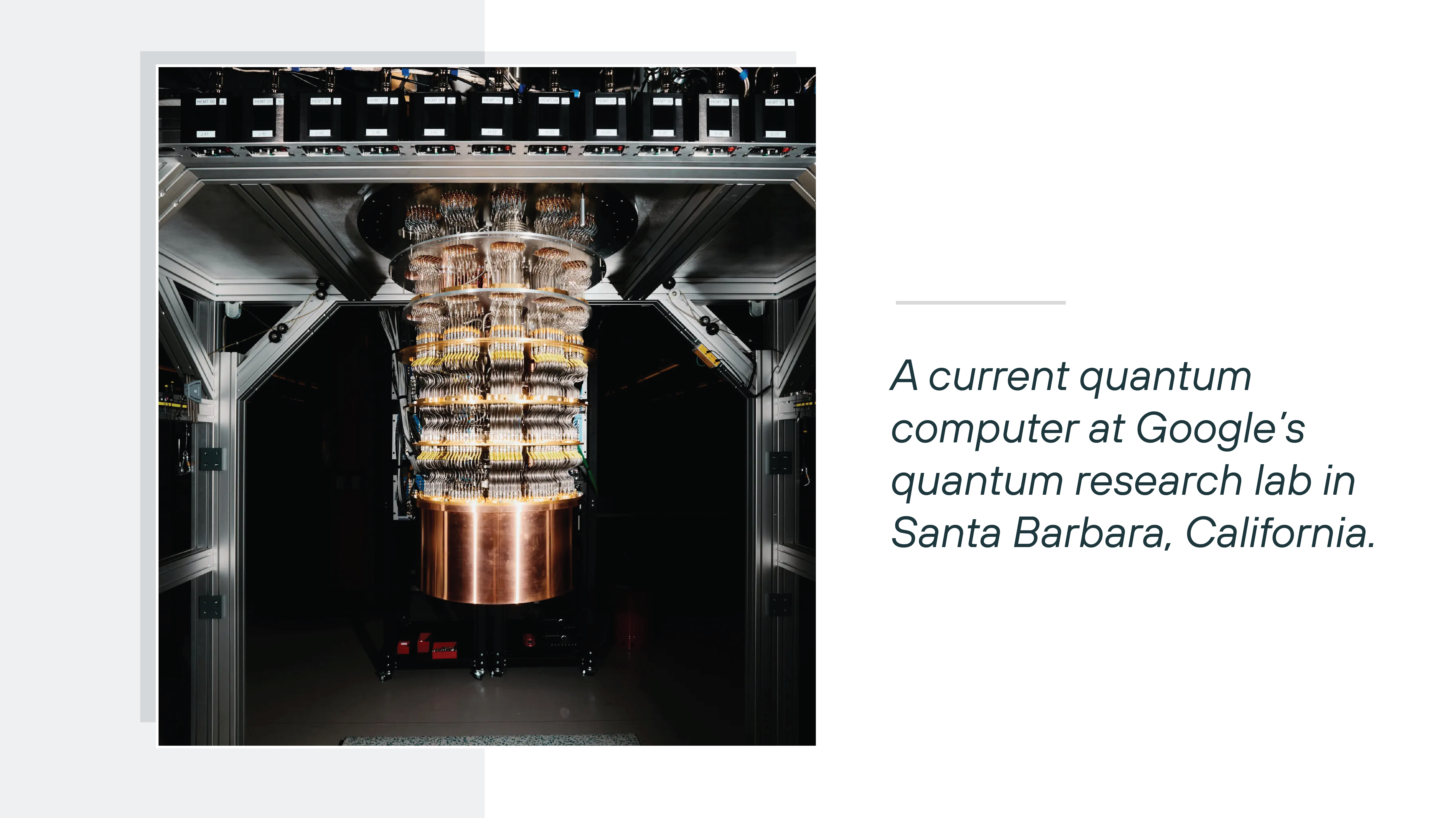 A large, vertically suspended quantum computing apparatus hangs at the center of a metallic laboratory frame, with multiple stacked circular tiers made of copper and gold-colored components connected by intricate wiring and cooling structures. The surrounding environment is dim, with structural beams, cables, and equipment framing the system. To the right, dark green text on a white background reads 'A current quantum computer at Google's quantum research lab in Santa Barbara, California.'