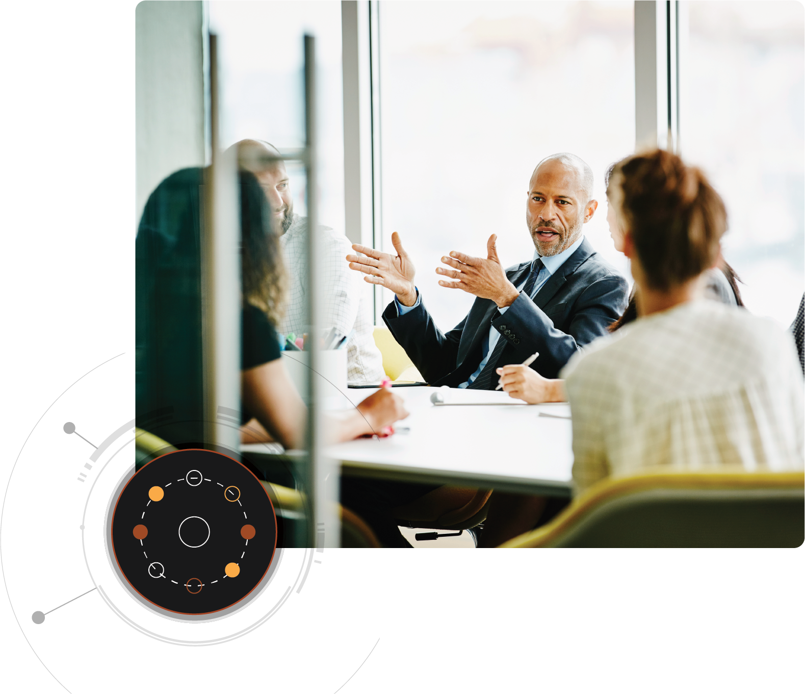 A man is speaking to several people sitting around a conference table with a circle graphic overlay in the bottom left corner.